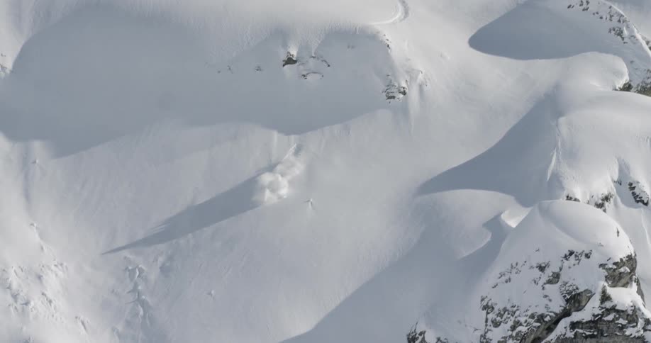 A skier jumps over a mound of fresh snow on an off piste run before landing awkwardly