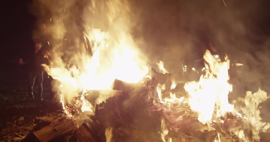 An outdoors bonfire burns and smokes