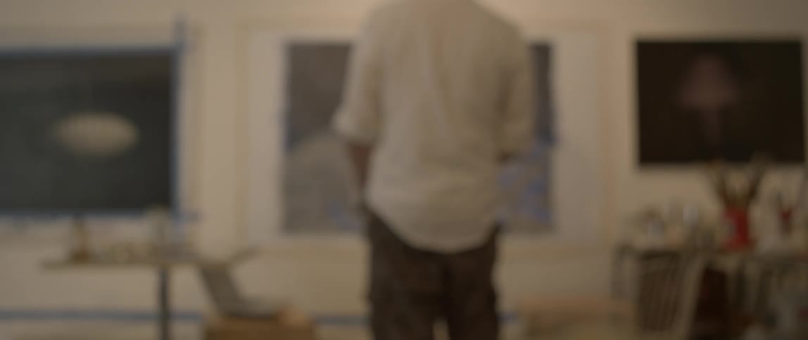 A painter works on his painting that is hanging on a wall