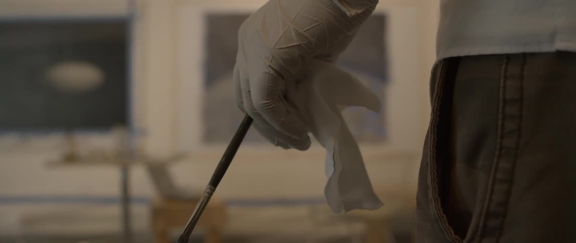 A person with a glove on their hand holds a paintbrush
