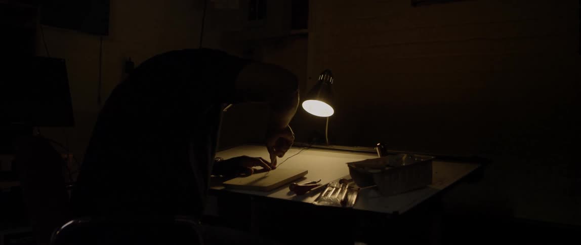 A craftsman in a dark room working a block of wood