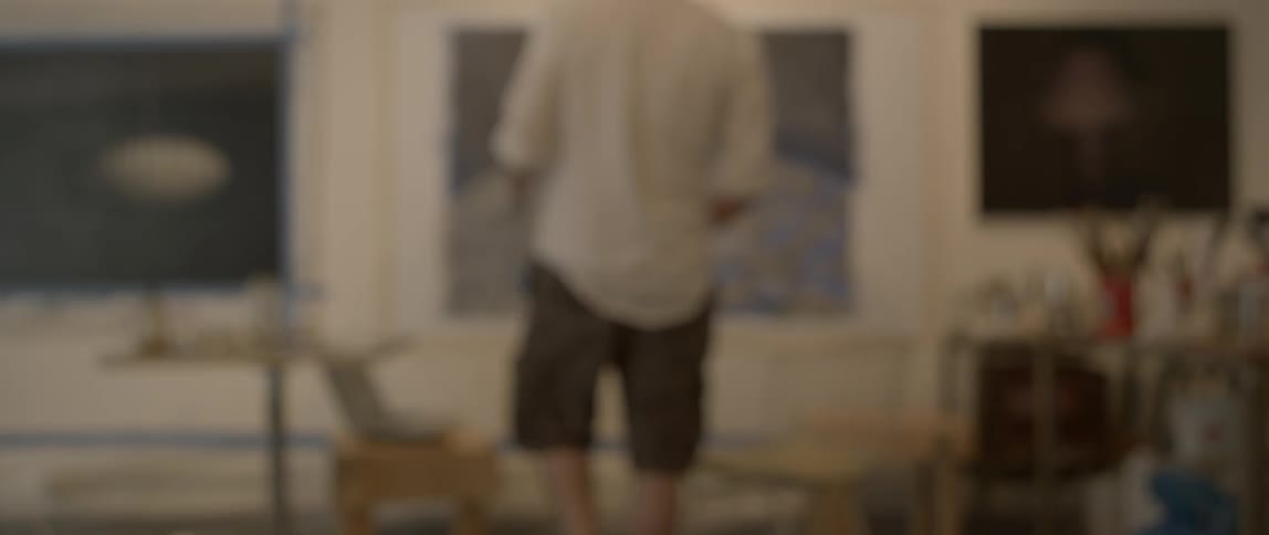 Man walks up to a painting as he holds a paintbrush