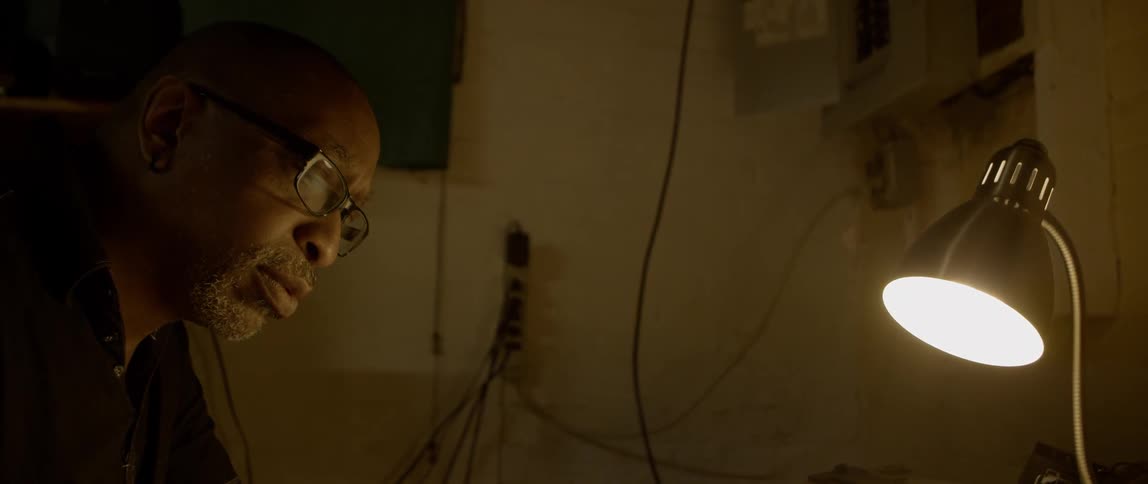 Black man in glasses sits near the table lamp