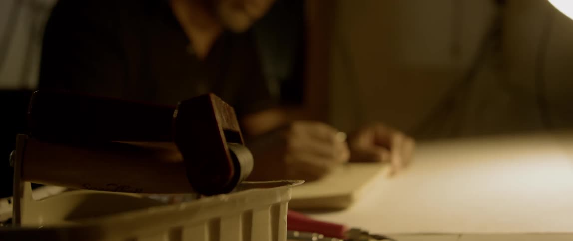 A man is carefully drawing a sketch with pencil on top of a wooden board as the basis of a carving he will make