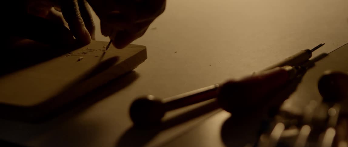 An artist uses a hand tool to carve and chisel a design into wood