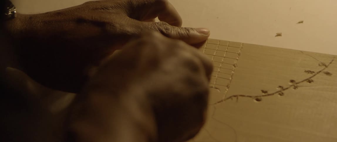 A person is using a tool to carve the surface of a piece of wood in order to create a piece of artwork