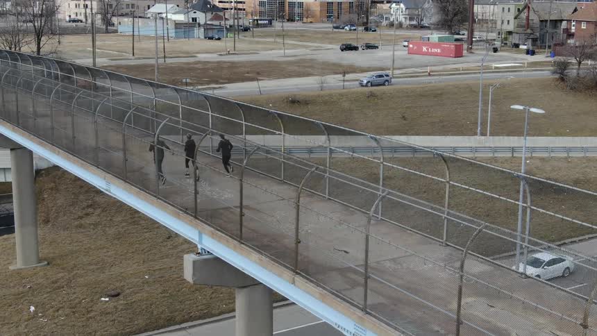 Three people jog down a fenced in pedestrian bridge above a highway