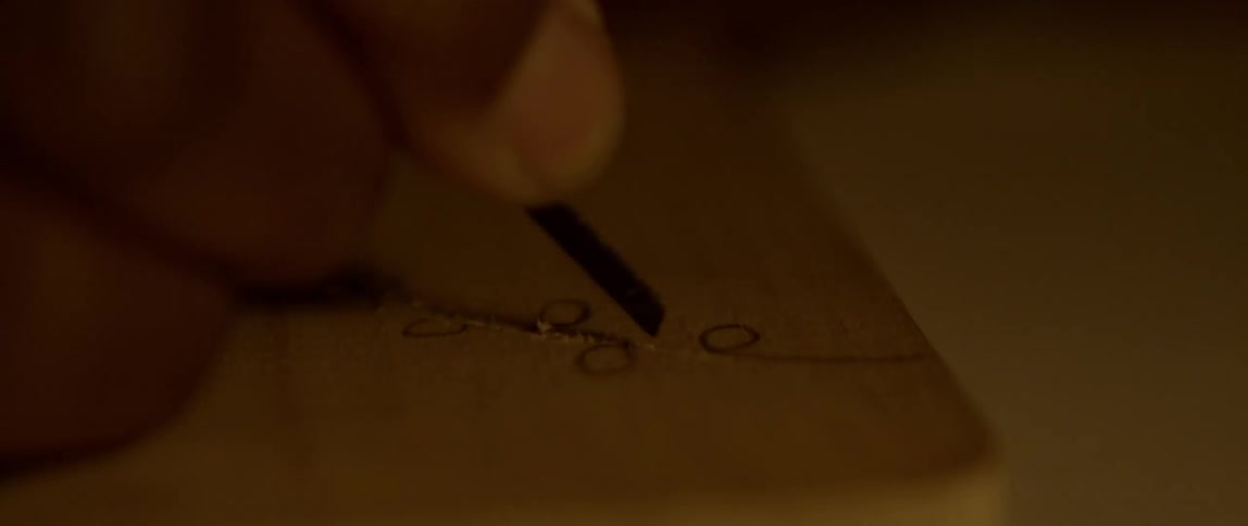 Artist carving a design on wood with a file