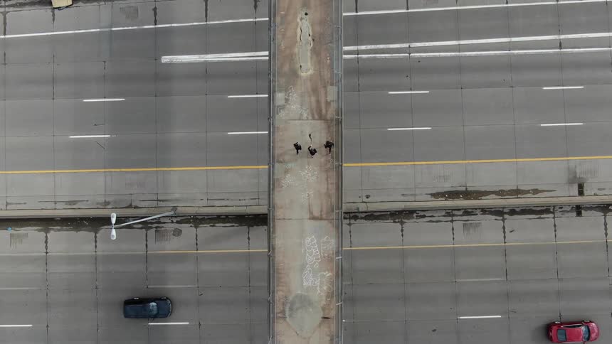 Three people run across a bridge above cars
