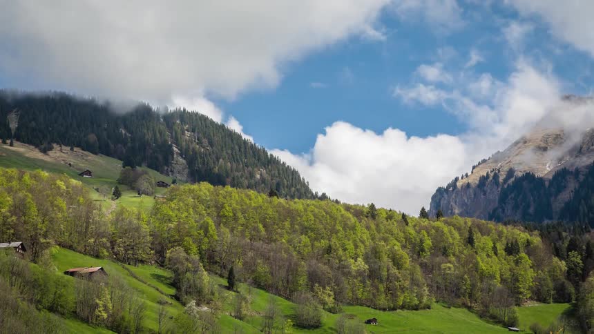 Landscape of a countryside valley between two mountains with green forest hills on a partly cloudy day