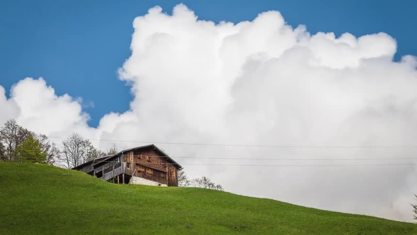 Clouds roll over a house on top of a grassy hill