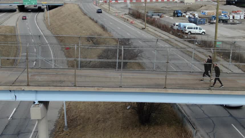 Three people walk across a pedestrian bridge over highway