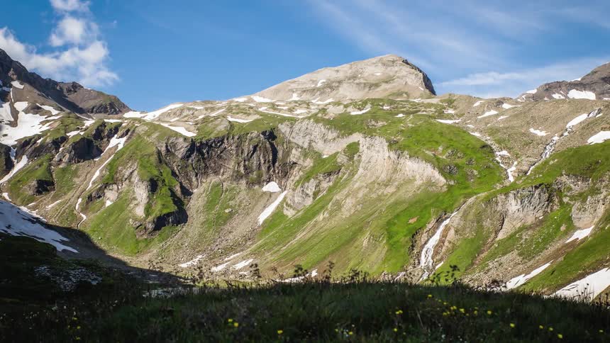 A time lapse of wind blowing the heather on a mountain side with a mountain right partially coveredby snow in the background