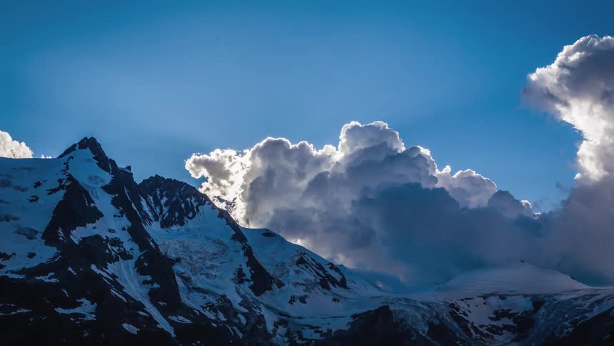 A time lapse of clouds dispersing on a snow capped rocky mountainous ridge