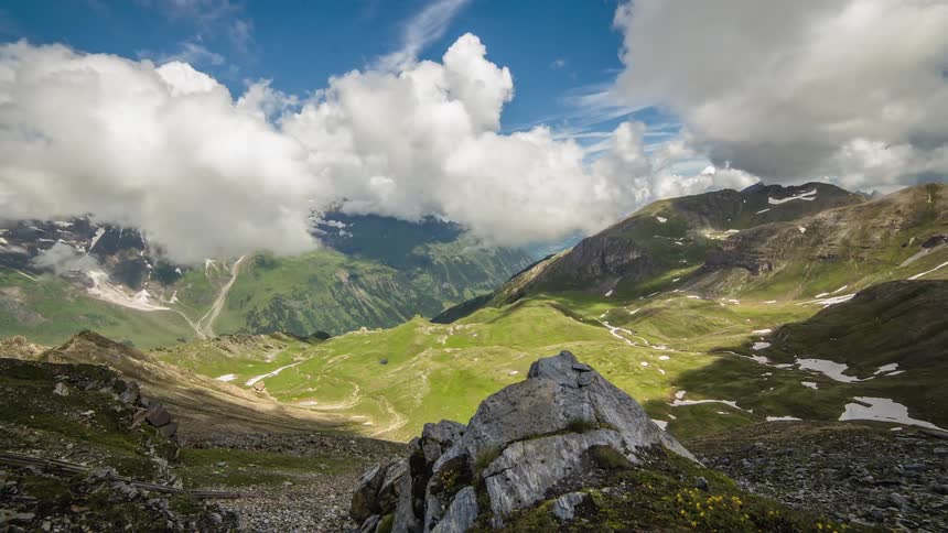 Clouds cast dark shadows on a grass covered mountain valley