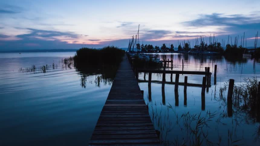 Sailboats float near a dock on a lake at sunset