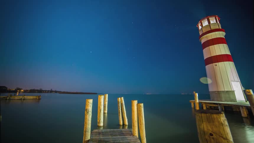 Timelapse of lighthouse on wooden pier at night