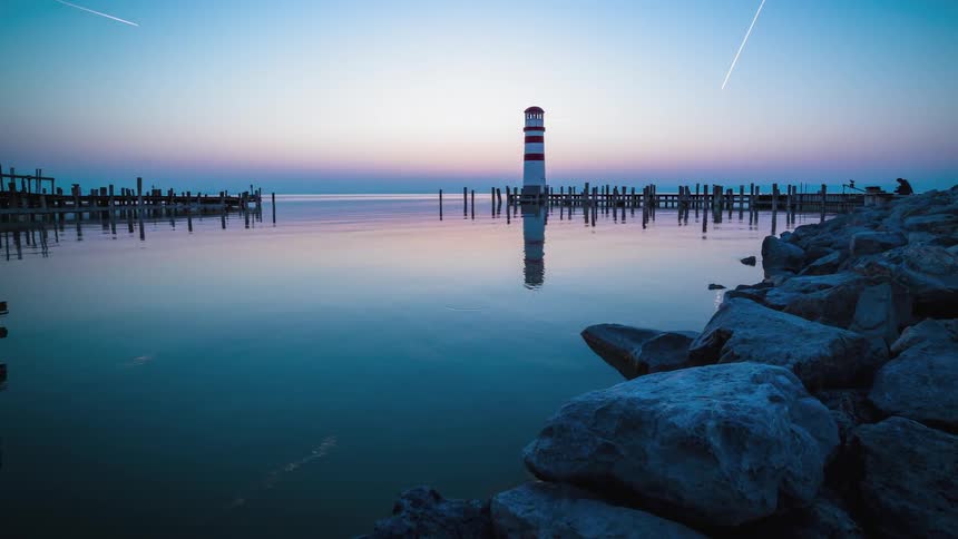Fisherman on piers checking their fishing lines thought the day while ducks swim by as the sunsets and the lighthouse lights up