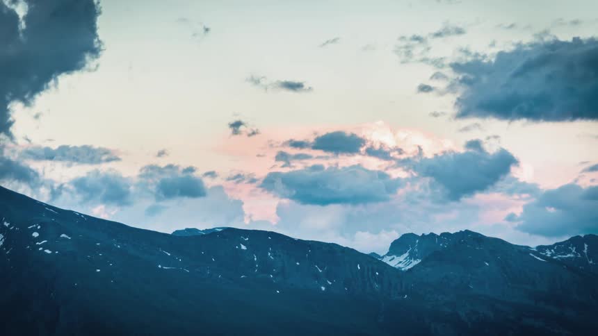 Clouds move in the sky above mountain tops