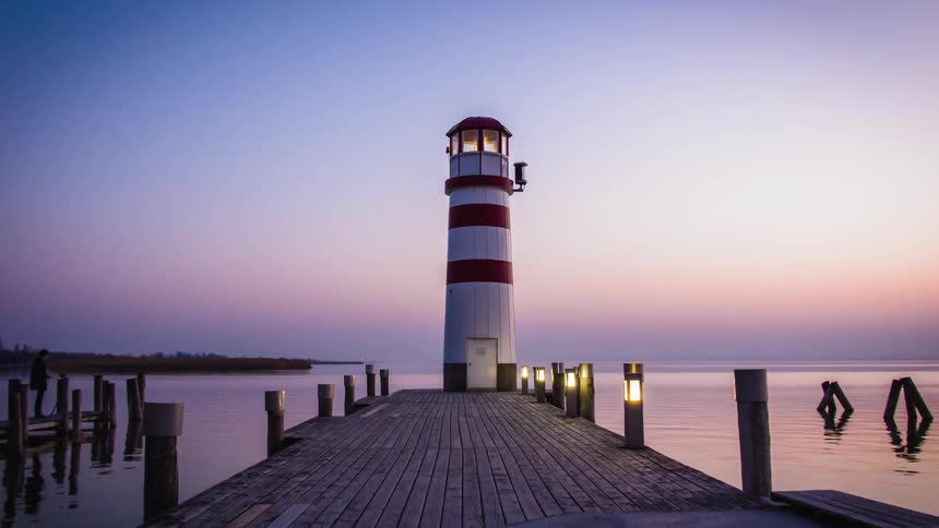 Timelapse of a lighthouse and pier on the shore of a lake at dusk