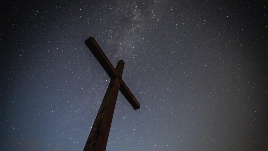 Shooting stars and clouds pass over tall wooden cross