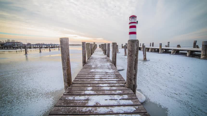 Two docks and a lighthouse sit by an ice covered waterway