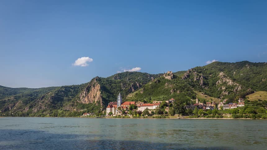 Multiple boats sail in front of a small mountain village
