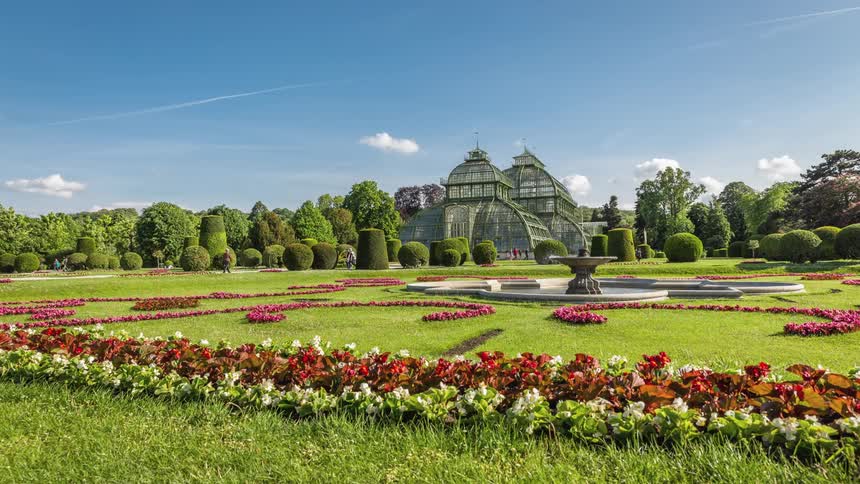 People walk through beautifully manicured gardens and past a fountain on a sunny day