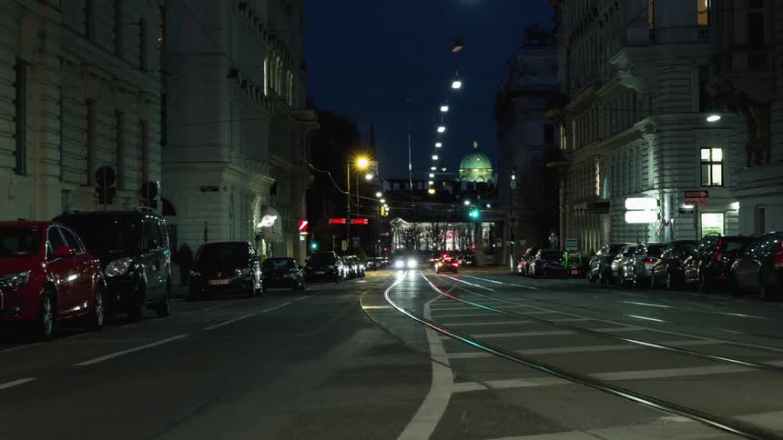 Cars and trains travel a busy city street at night