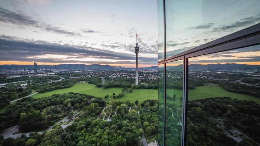 The clouds sky park and roads are reflected on the glass facade of a building at sunset