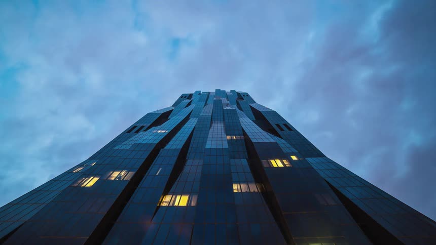 A sky scraper with a zig zagged glass cladding as the clouds pass above