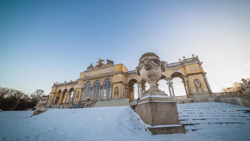 Pedestrians walk past a staircase that leads to an ornate building