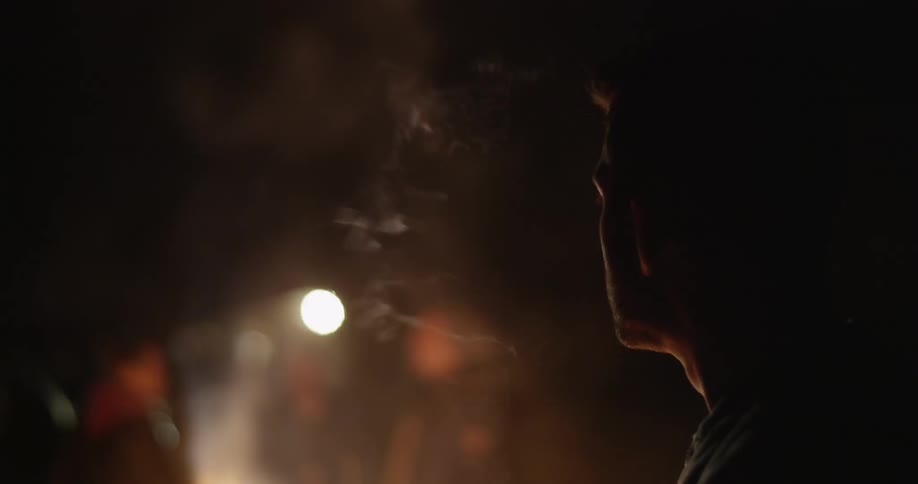 A man smokes in front of a bonfire