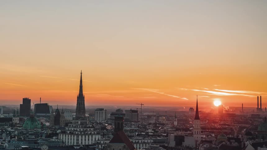Steeples buildings and smoke stacks stand tall over the city as the sun rises on the horizon