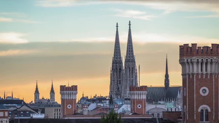Two gothic spires stand tall in the skyline of a medieval european city at sunset