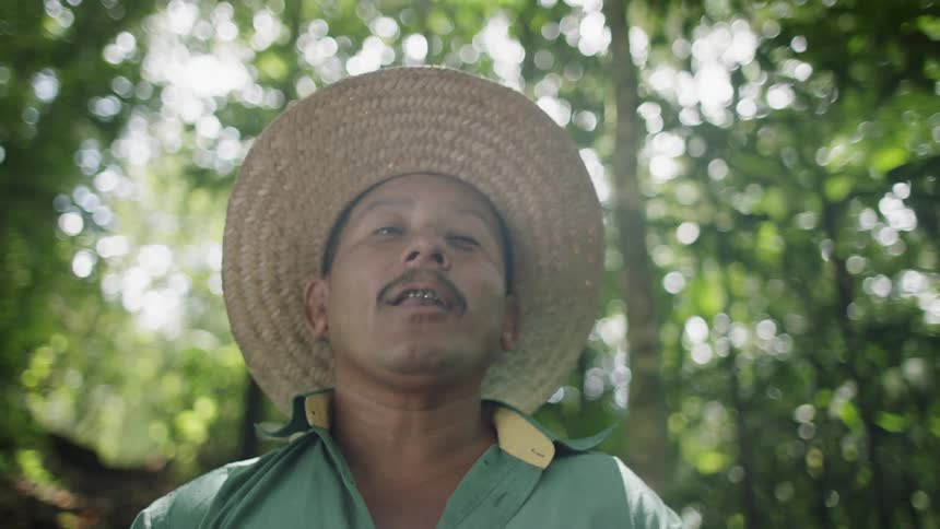 A man wearing a wicker hat is talking in the forest