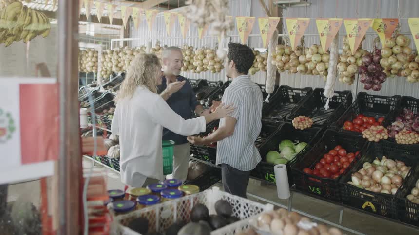 Two men and a woman at a produce store with crates filled with a variety of produce