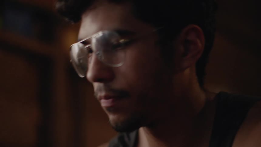 Brunette man wearing glasses contemplates and puts his hand over his mouth indoors during daylight