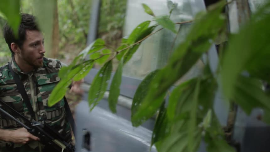 A man with a gun approaches a jeep in the woods and pulls the occupant out