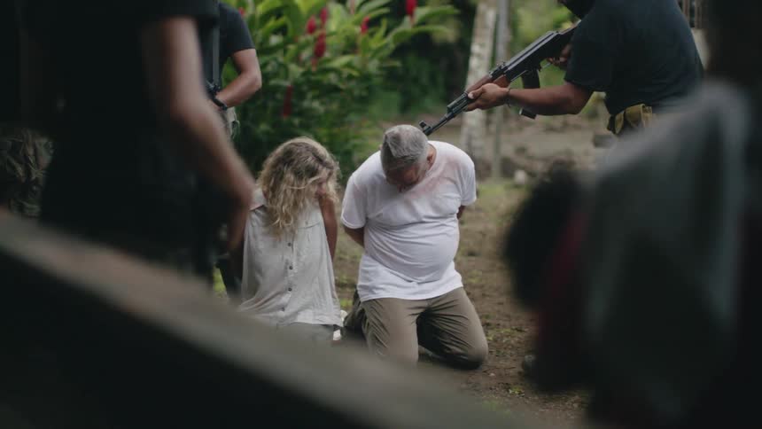 Armed men in camouflage point guns at kneeling couple