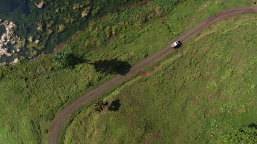 A car travels along a road by a grassy field