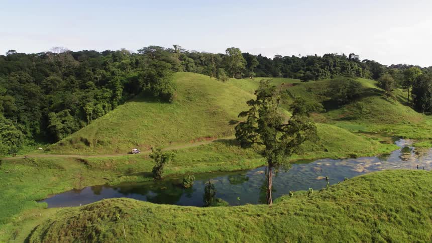 A car drives along a winding road through lush green hills