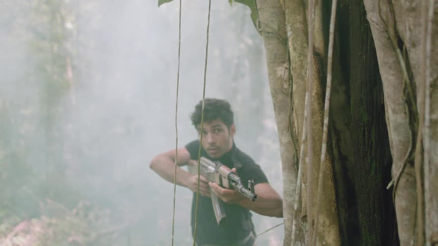 A man turns a the corner of a tree with an automatic weapon