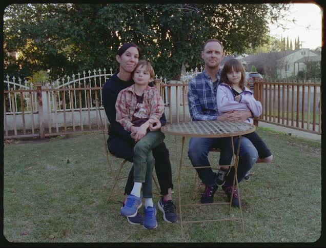 A white family sits a table in a fenced in yard and poses for a picture