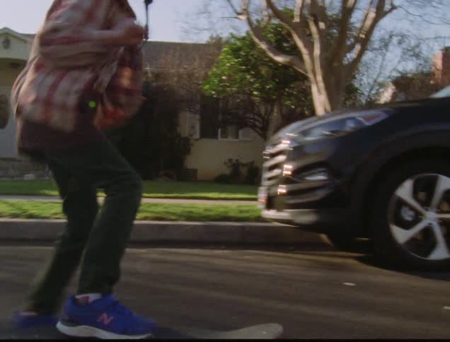 A young boy wearing a helmet rides a skateboard down the middle of the street in a suburban neighborhood