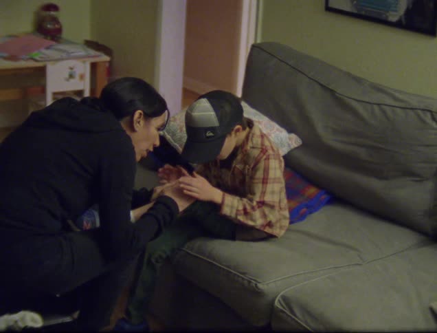 A mother consoles her son as he sits on the couch in the family room showing her a spot on his knee that is upsetting him