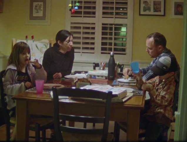 A family of four is gathered at the dinner table talking while the father and daughter finish eating their meal