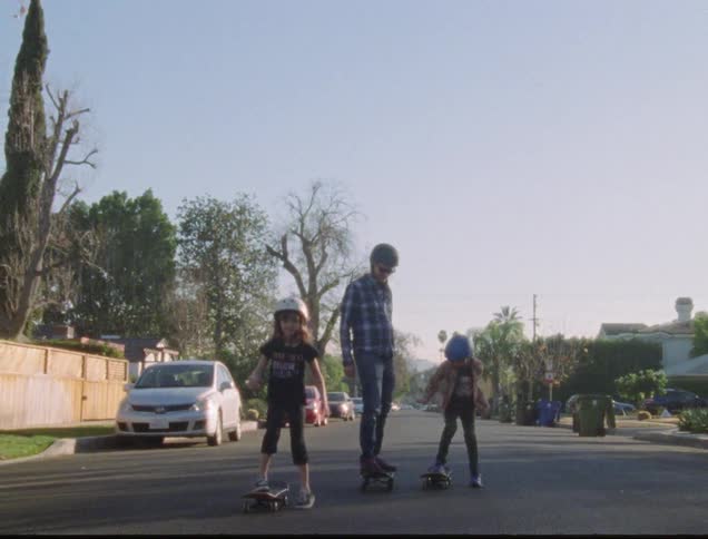 A father and children skateboard down a neighborhood street