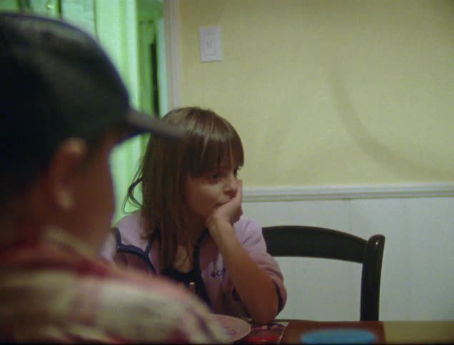 A family at the dinner table having a dominoes pizza as the daughter shrugs her shoulders before speaking