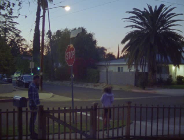 A young girl jumps up and down on a pogo stick as her father watches and her brother rushes to join